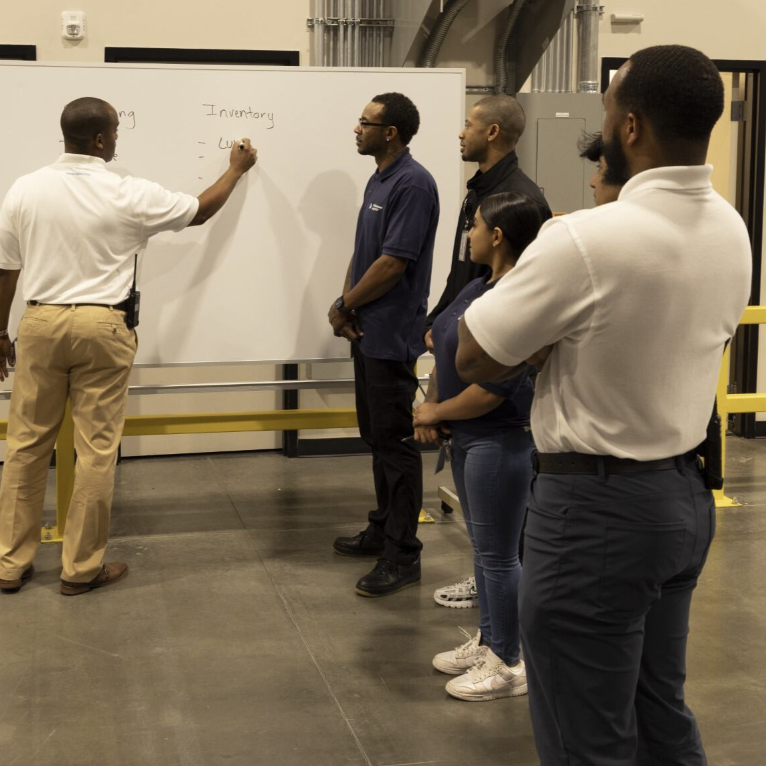 African American Male Team Leader Writing on Whiteboard and Discussing with Racially Diverse Employees at LSL Warehouse